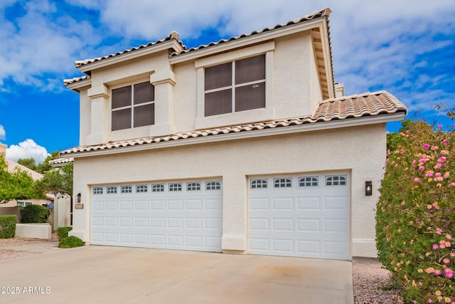 mediterranean / spanish-style home featuring a tile roof, stucco siding, an attached garage, and concrete driveway