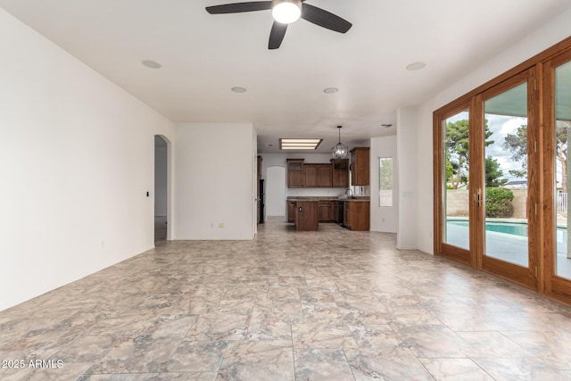 unfurnished living room with arched walkways, ceiling fan, and a sink