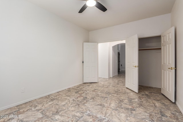 unfurnished bedroom with a ceiling fan, baseboards, arched walkways, and a closet