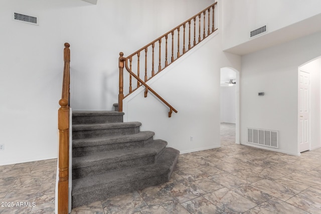 stairs featuring visible vents, arched walkways, and a high ceiling