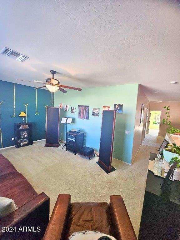 carpeted living room featuring ceiling fan and a textured ceiling