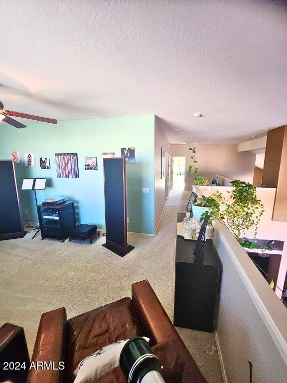 living room featuring ceiling fan, light colored carpet, and a textured ceiling