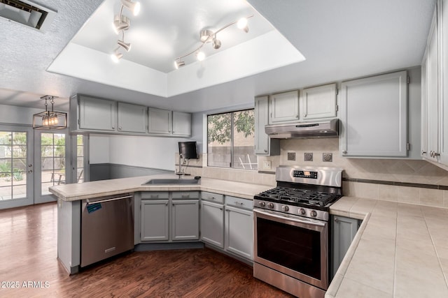 kitchen with visible vents, gray cabinets, under cabinet range hood, appliances with stainless steel finishes, and a peninsula