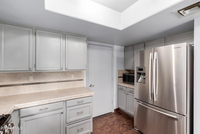 kitchen featuring visible vents, backsplash, tile counters, appliances with stainless steel finishes, and dark wood-style floors