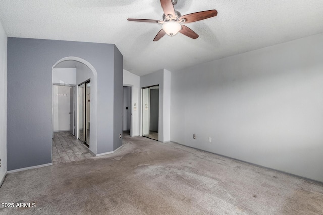 unfurnished bedroom featuring a textured ceiling, arched walkways, carpet floors, lofted ceiling, and ceiling fan