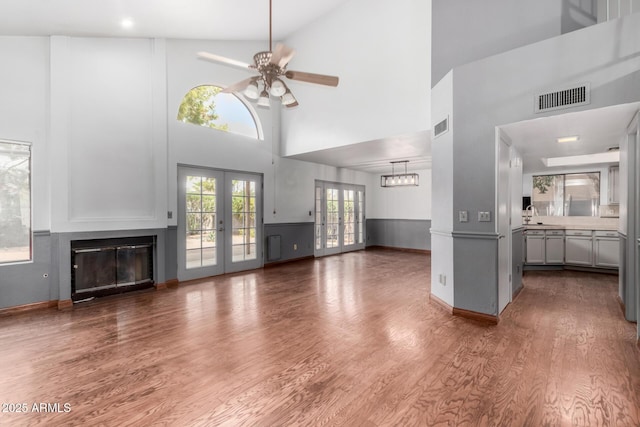 unfurnished living room featuring a glass covered fireplace, visible vents, wood finished floors, and french doors