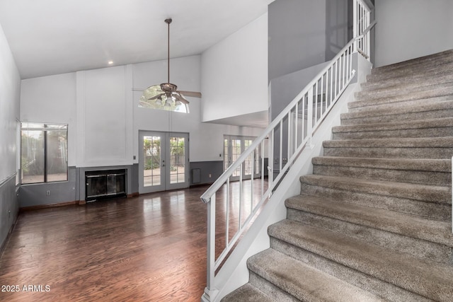 stairway featuring a ceiling fan, wood finished floors, a high ceiling, french doors, and a glass covered fireplace