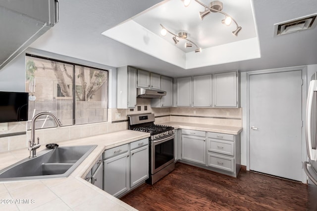 kitchen with stainless steel gas range oven, visible vents, under cabinet range hood, a tray ceiling, and a sink