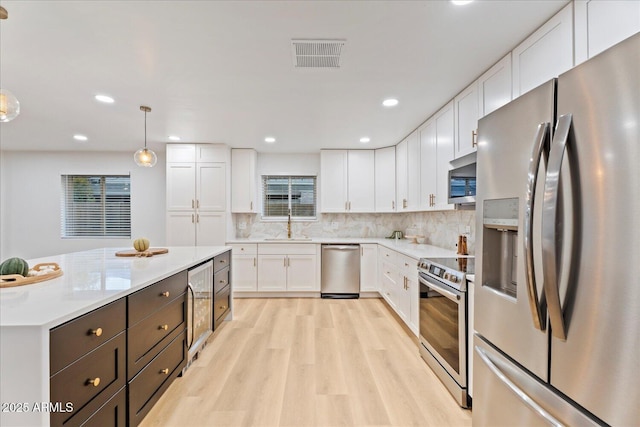 3506 W Yucca St, Phoenix, AZ 85029 - kitchen with appliances with stainless steel finishes, white cabinets, light wood-style flooring, light countertops, and decorative light fixtures
