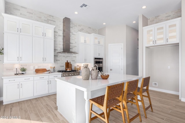 kitchen featuring white cabinetry, a kitchen island with sink, a breakfast bar area, and wall chimney exhaust hood