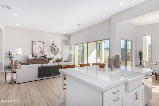 kitchen with light hardwood / wood-style flooring, sink, a center island with sink, and white cabinets