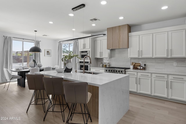 kitchen with decorative light fixtures, light stone counters, white cabinetry, and an island with sink