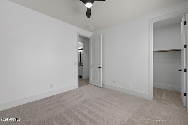 unfurnished bedroom with a spacious closet, a closet, ceiling fan, and light colored carpet