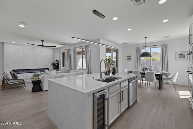 kitchen with sink, beverage cooler, an island with sink, pendant lighting, and light hardwood / wood-style floors