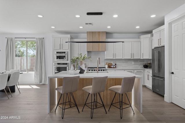 kitchen with white cabinets, a kitchen breakfast bar, decorative backsplash, an island with sink, and appliances with stainless steel finishes