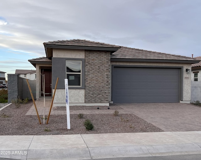 prairie-style house featuring an attached garage, a tiled roof, decorative driveway, and stucco siding