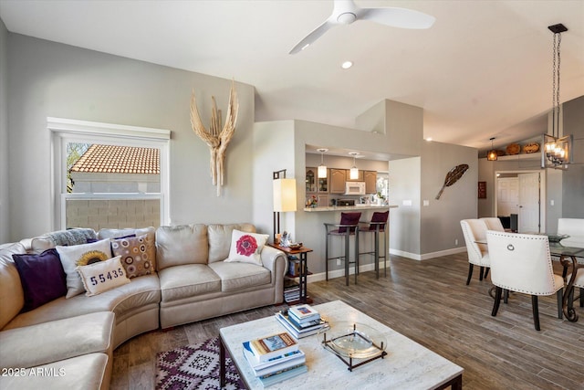 living area featuring lofted ceiling, baseboards, dark wood-style flooring, and ceiling fan with notable chandelier