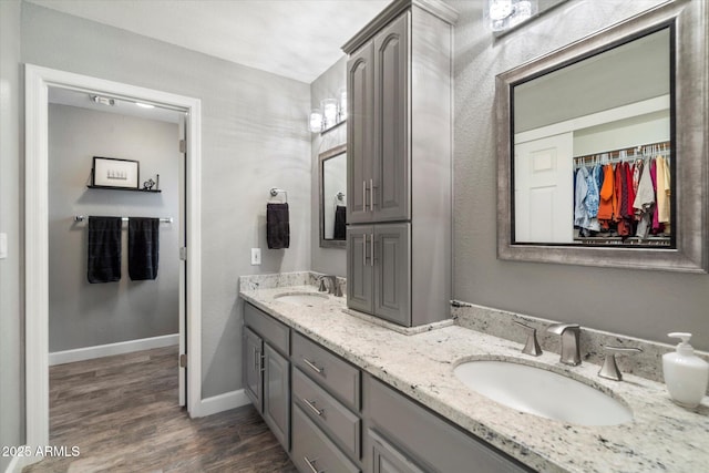 full bath with double vanity, wood finished floors, a sink, and baseboards