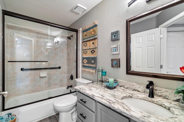 full bathroom featuring a textured wall, bath / shower combo with glass door, vanity, and toilet