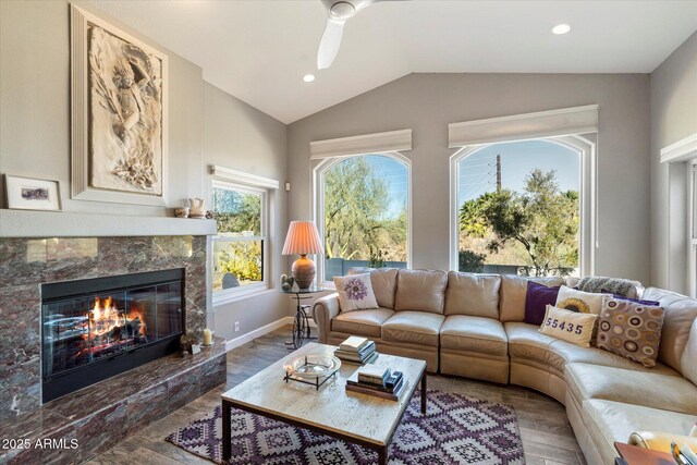 living area with baseboards, lofted ceiling, ceiling fan, wood finished floors, and a fireplace