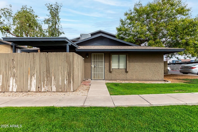 view of front of property featuring roof with shingles, a front yard, fence, and stucco siding