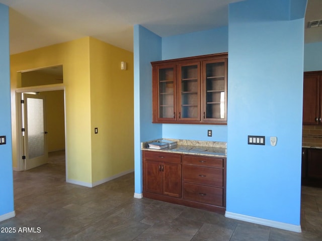 kitchen with visible vents, light stone countertops, glass insert cabinets, baseboards, and tasteful backsplash