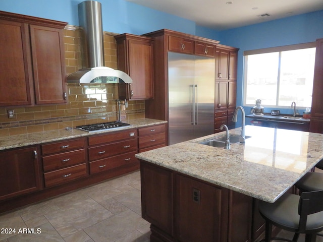 kitchen with decorative backsplash, an island with sink, extractor fan, light stone countertops, and stainless steel appliances