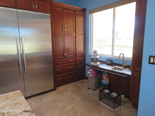 kitchen with stainless steel built in fridge, sink, and light stone counters