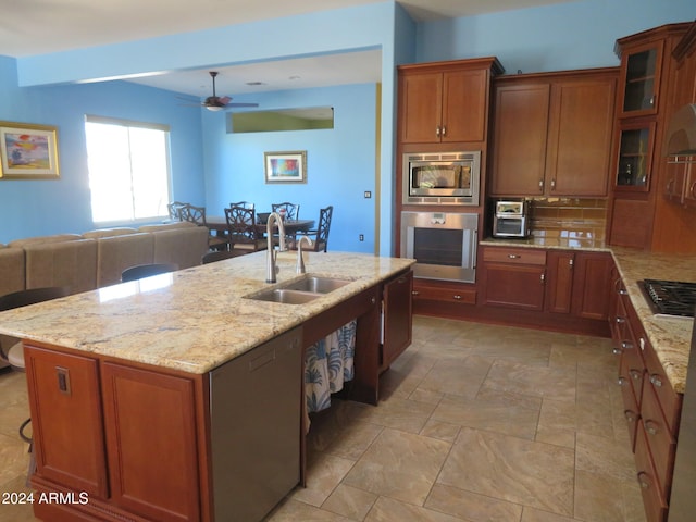 kitchen featuring a center island with sink, sink, appliances with stainless steel finishes, light stone counters, and tasteful backsplash