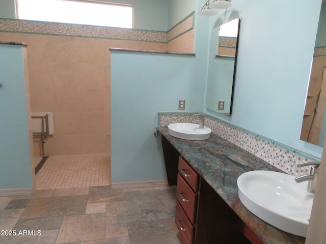 bathroom featuring a sink, a walk in shower, baseboards, and double vanity