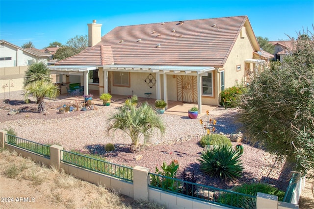 rear view of house with stucco siding, a chimney, fence private yard, and a tile roof