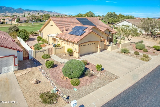 mediterranean / spanish house with a tile roof, a garage, stucco siding, a gate, and solar panels