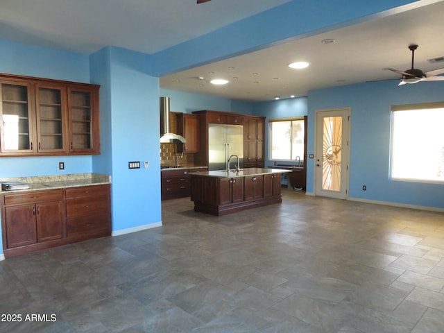 kitchen with a kitchen island with sink, ceiling fan, stainless steel built in fridge, and a wealth of natural light