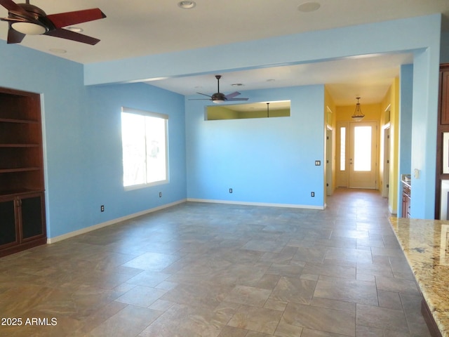 unfurnished living room with baseboards, a ceiling fan, and stone finish flooring