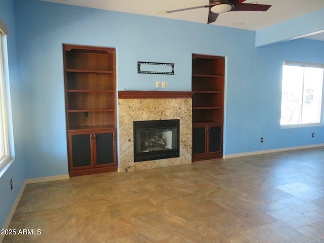 unfurnished living room with baseboards, a ceiling fan, built in features, and a premium fireplace