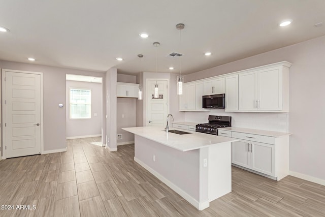 kitchen featuring black range with gas stovetop, sink, pendant lighting, white cabinetry, and an island with sink