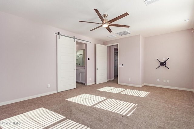 unfurnished bedroom with light carpet, a barn door, ensuite bathroom, and ceiling fan