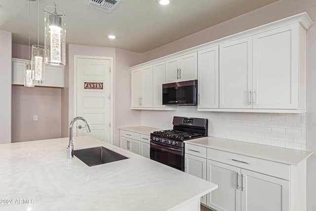 kitchen featuring black gas range oven, white cabinetry, hanging light fixtures, and sink