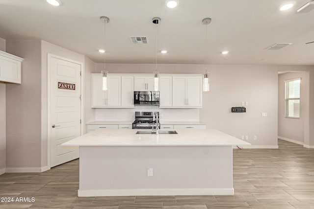 kitchen with white cabinets, appliances with stainless steel finishes, pendant lighting, and an island with sink