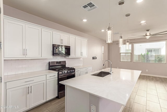 kitchen with gas stove, white cabinetry, sink, hanging light fixtures, and a kitchen island with sink