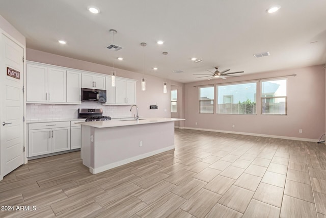 kitchen with ceiling fan, stainless steel range with gas cooktop, sink, and an island with sink