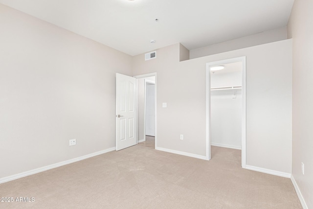 unfurnished bedroom with a spacious closet, a closet, and light colored carpet