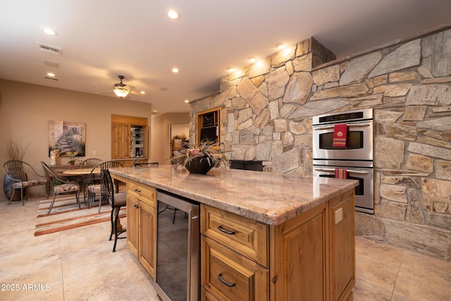 kitchen with a breakfast bar, a center island, stainless steel double oven, beverage cooler, and light stone countertops