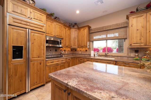 kitchen with sink, light tile patterned floors, light stone counters, paneled fridge, and decorative backsplash