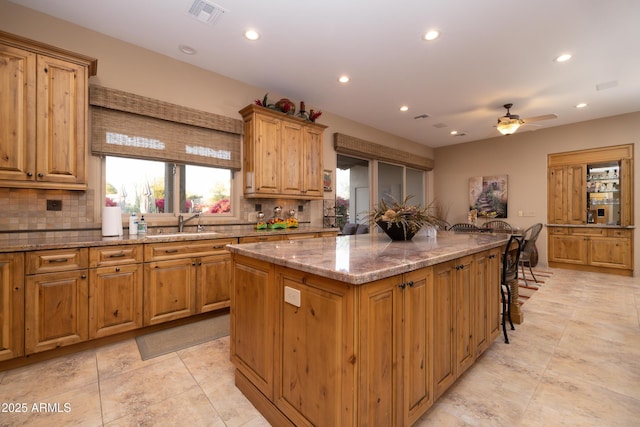 kitchen with a kitchen bar, sink, light stone counters, tasteful backsplash, and a center island