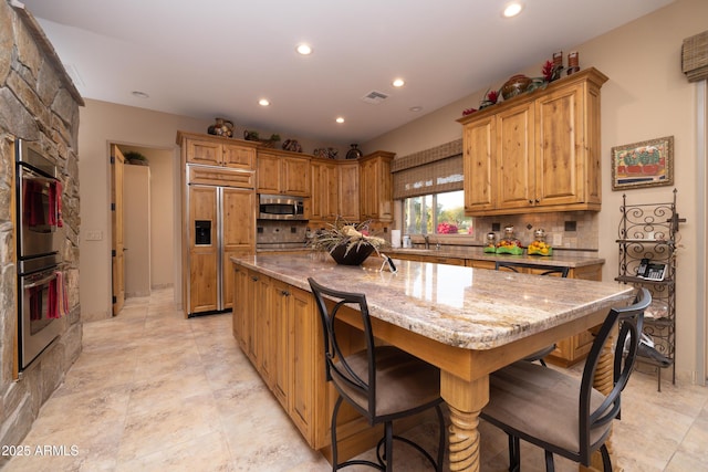 kitchen with a kitchen bar, light stone counters, a kitchen island, stainless steel appliances, and decorative backsplash