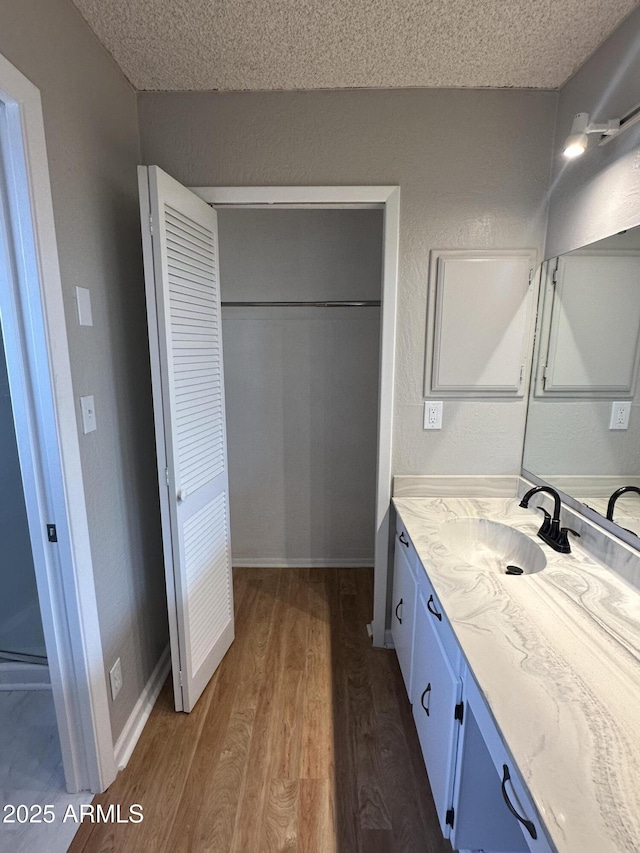 bathroom featuring baseboards, a textured ceiling, vanity, and wood finished floors