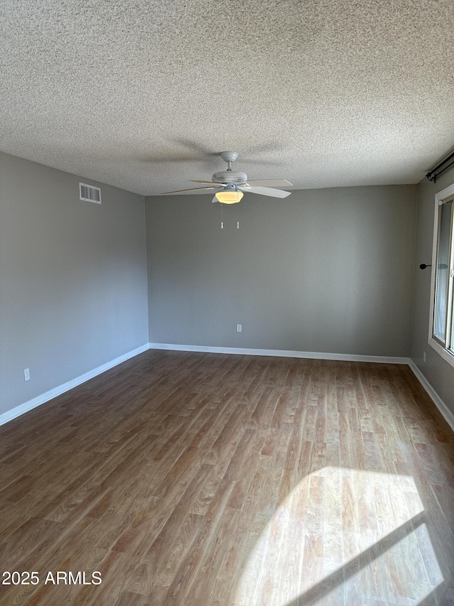 empty room with wood finished floors, visible vents, and baseboards