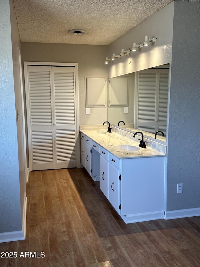 bathroom with double vanity, a textured ceiling, a sink, and wood finished floors