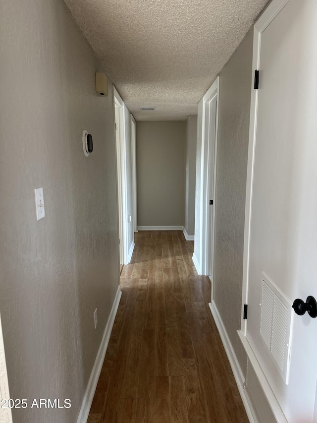 hall featuring baseboards, visible vents, a textured wall, dark wood-type flooring, and a textured ceiling